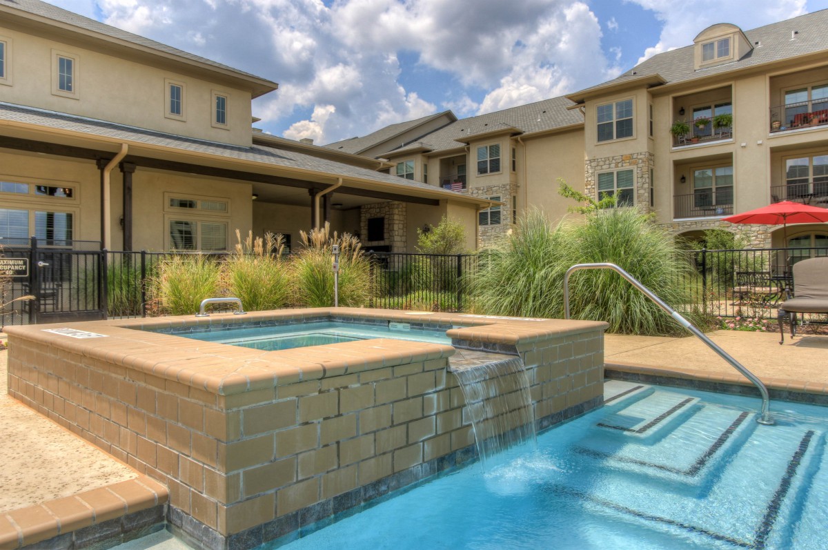 A residential building with a pool and spa, surrounded by landscaping under a partly cloudy sky.