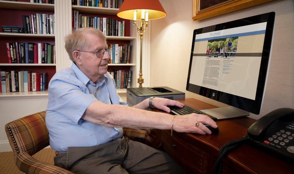 An elderly man using a computer at his desk in an office setting.