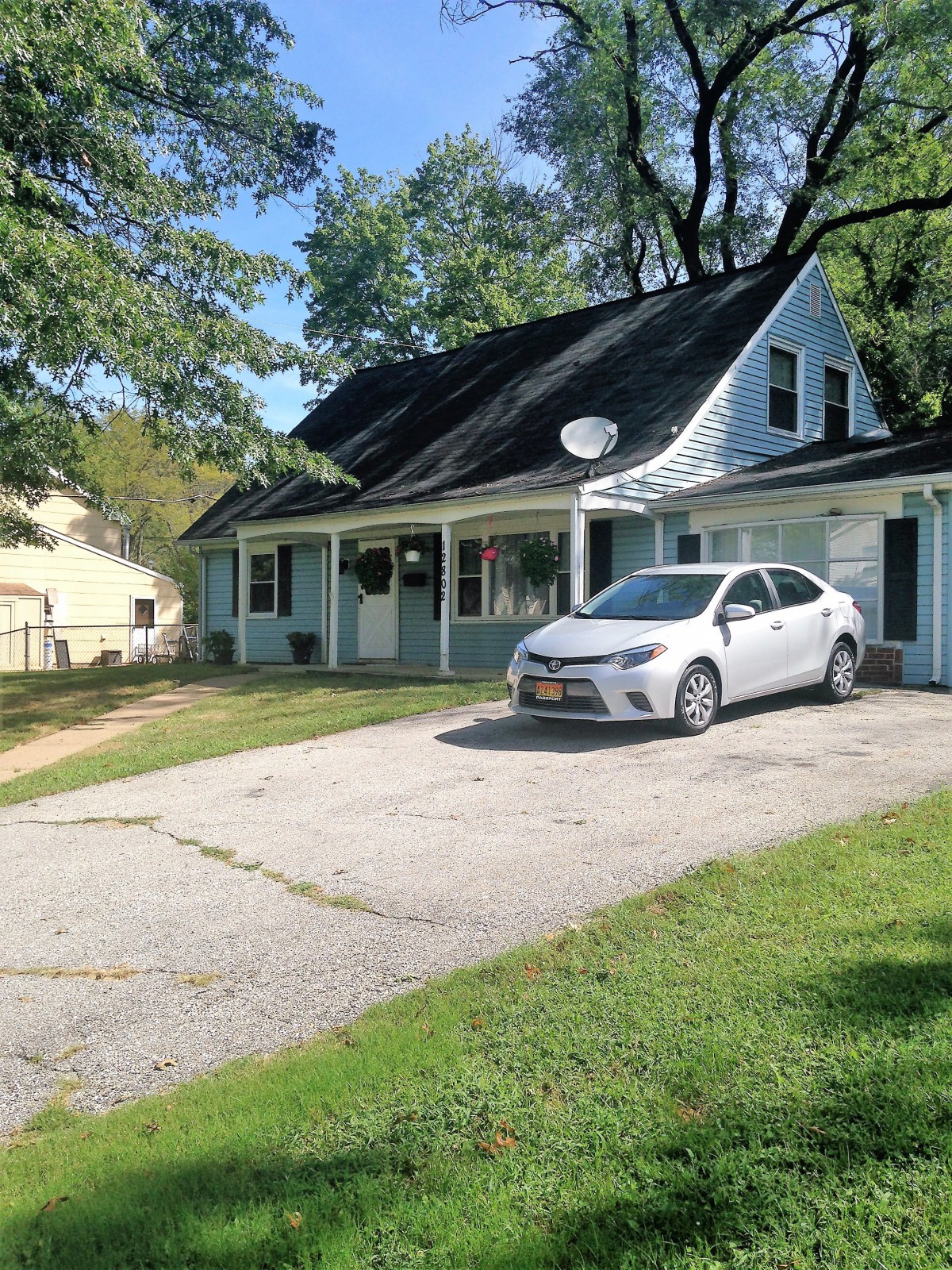 A residential house with a car parked in the driveway and surrounded by trees.
