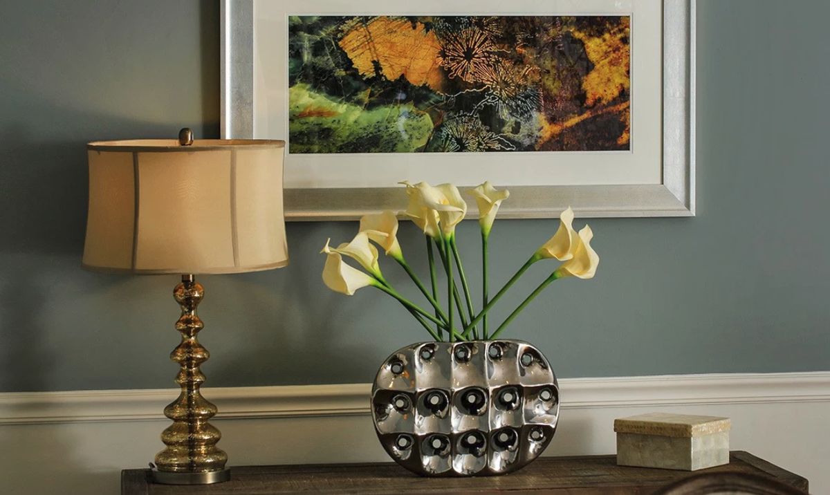 A stylish interior setup featuring a vase of calla lilies, a decorative lamp, and a framed artwork on the wall.