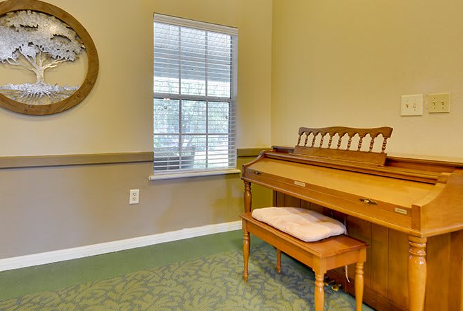 A cozy room featuring a wooden piano and a bench with a cushion next to a window.