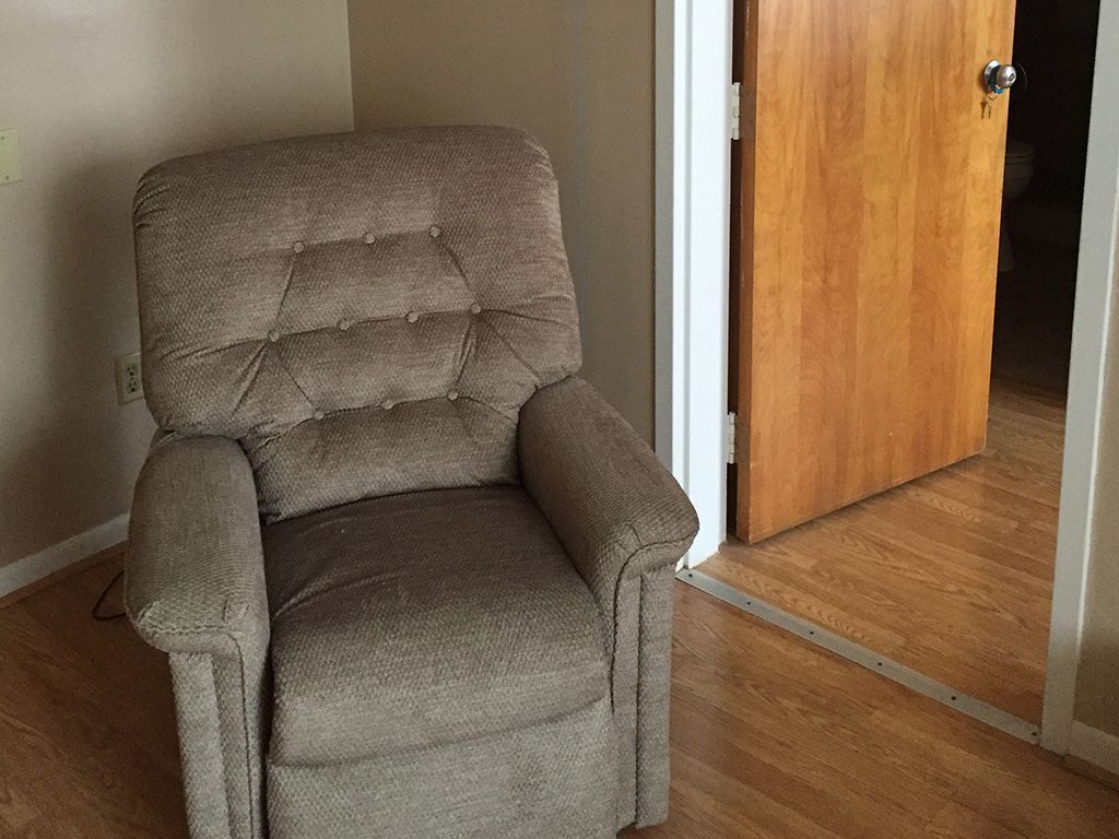 A comfortable recliner chair next to a wooden door on a hardwood floor.