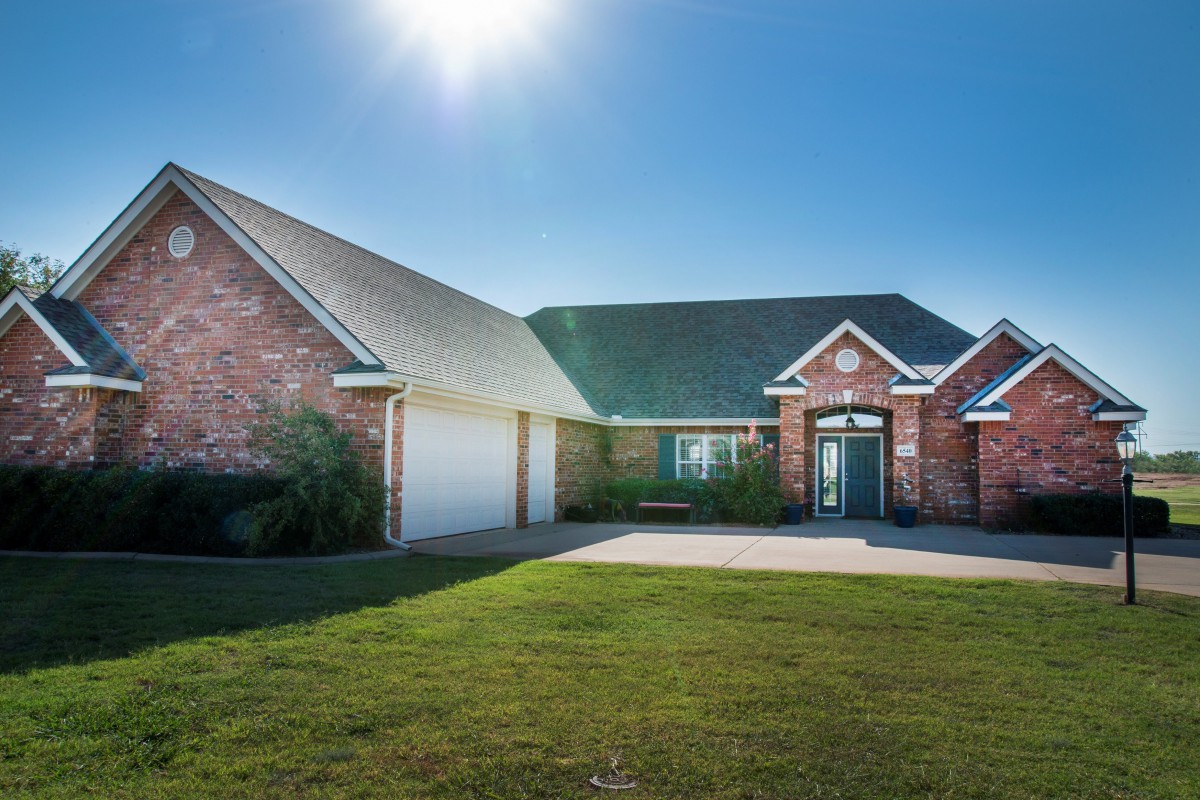 A sunny day view of a residential brick house with a driveway and a two-car garage.