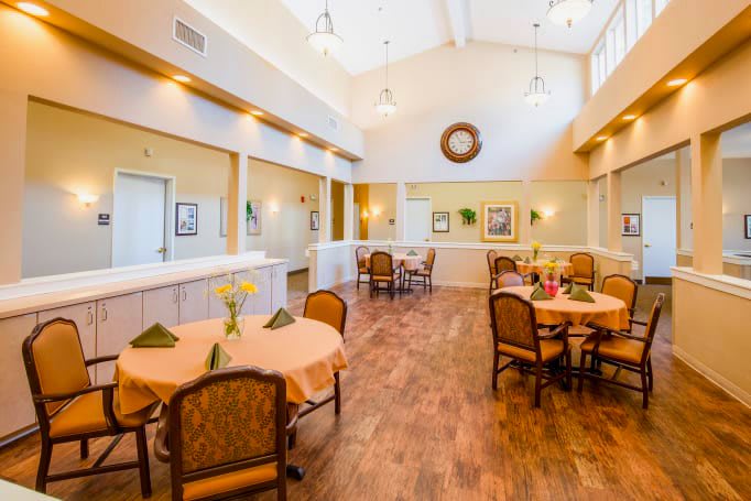 A well-lit dining area with neatly arranged tables and chairs, featuring decorative plants.