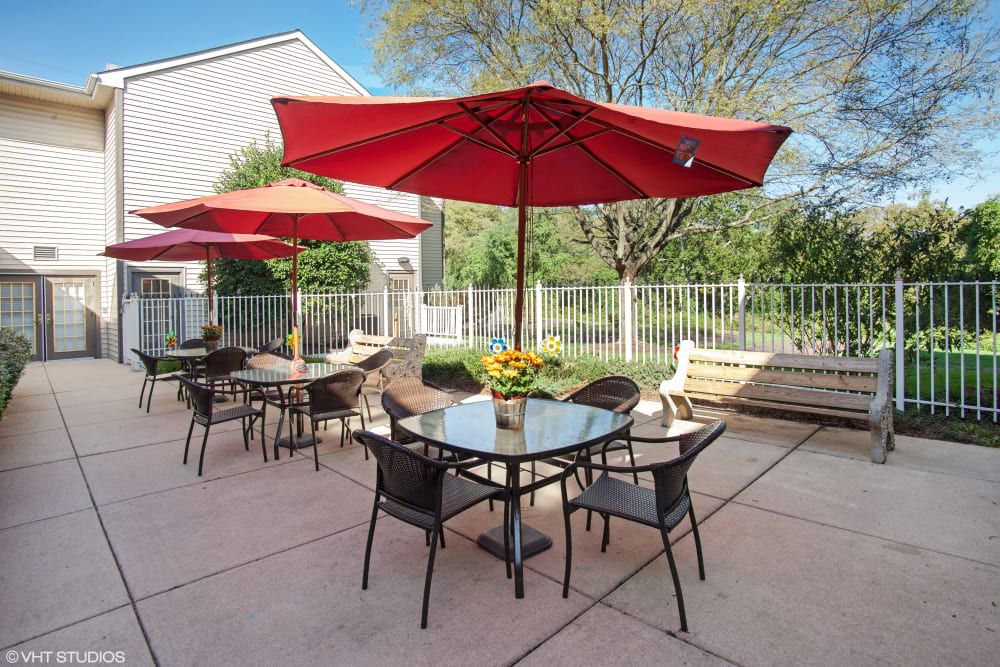 An inviting outdoor patio with tables, chairs, and vibrant red umbrellas set under a clear blue sky.