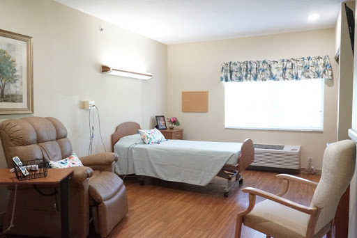A well-lit and organized patient room in a hospital, featuring a bed, seating area, and window.