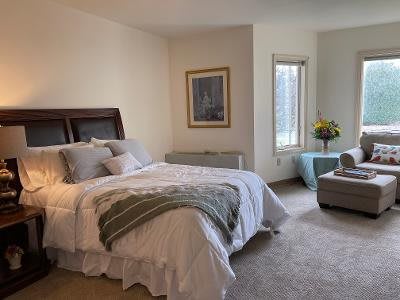 A cozy bedroom with a large bed, armchair, and window providing natural light.