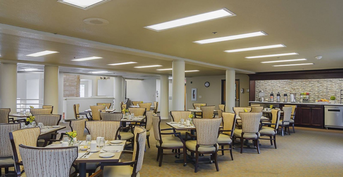 A spacious dining room with neatly arranged tables and chairs, well-lit by overhead lights.