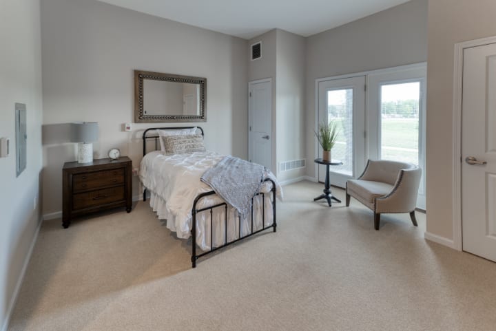 A cozy bedroom with a metal bed frame, nightstand, mirror, and chair by the window.