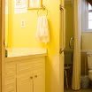 A brightly lit bathroom with yellow walls, featuring a vanity with a mirror and a hanging towel.