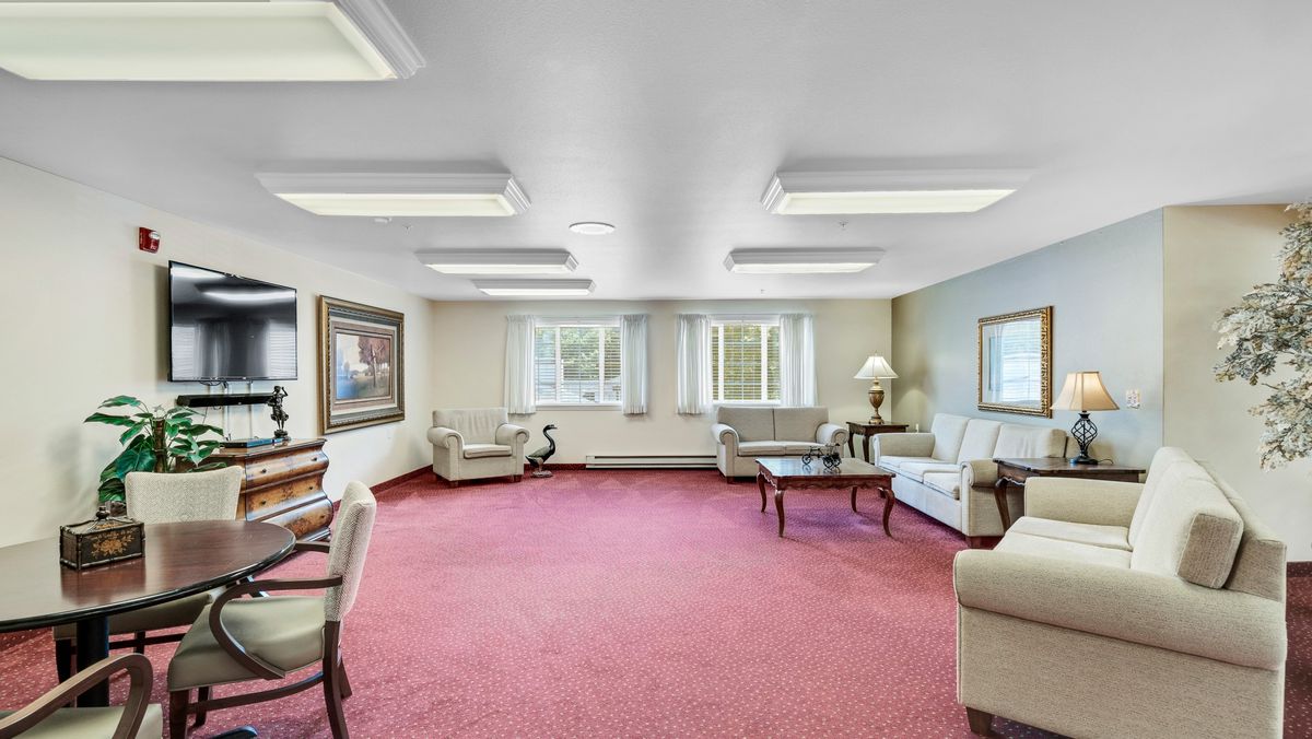 A spacious living room with comfortable sofas and a coffee table, featuring large windows and a carpeted floor.