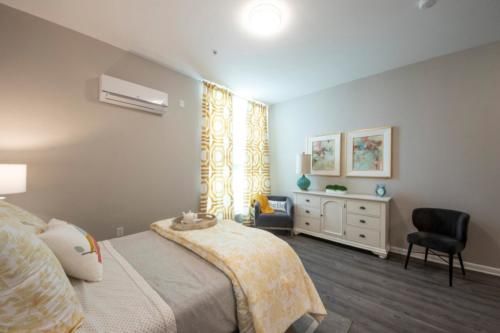 A modern bedroom featuring minimalist decor with neutral tones, a bed, and an air conditioner mounted on the wall.