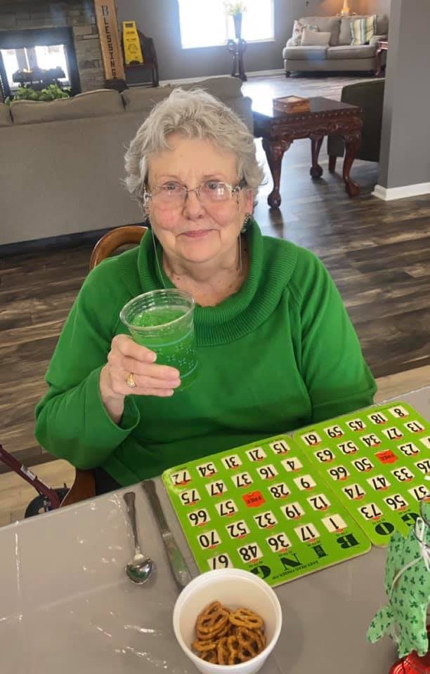 An elderly woman enjoys a green drink while playing bingo.