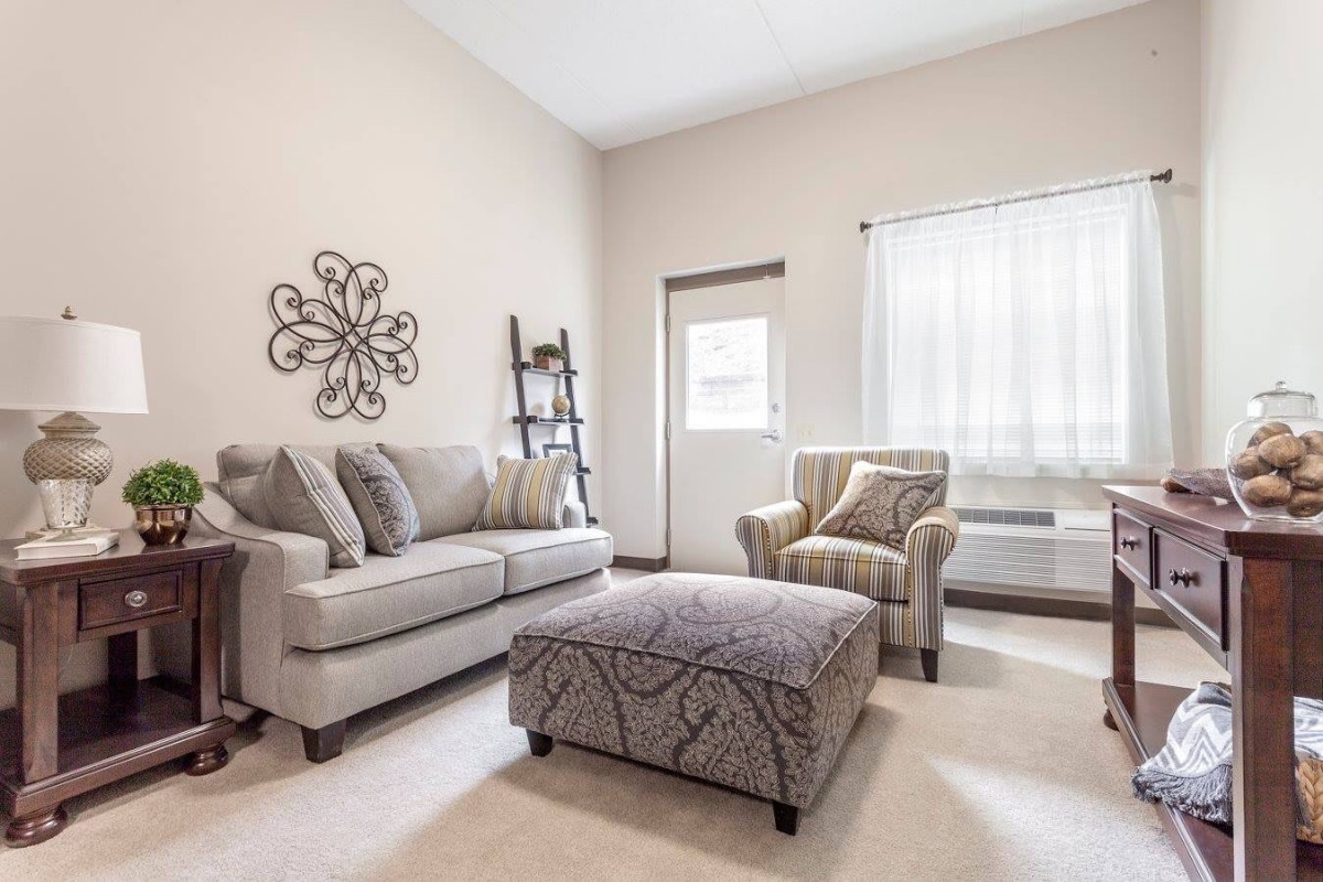 A cozy living room with a comfortable sofa, armchair, and ottoman arranged in a well-lit space.