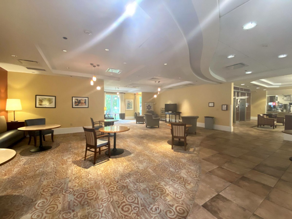A well-lit interior room with tables and chairs, adorned with artwork and carpeted flooring.
