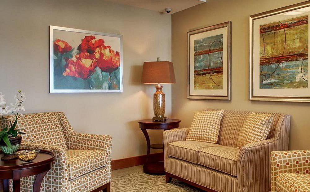A cozy living room corner with patterned sofas, a table lamp, and two pieces of artwork on the wall.