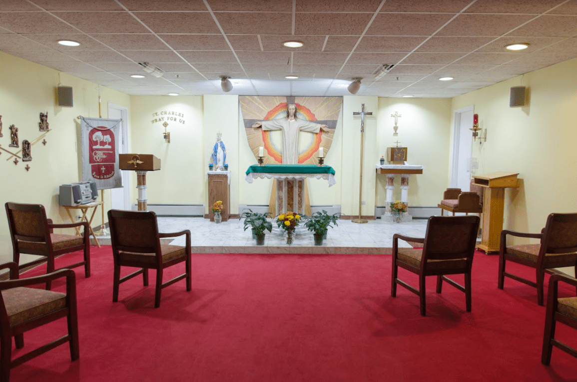 A chapel with an altar and crucifix, featuring red carpet and seating arrangements.