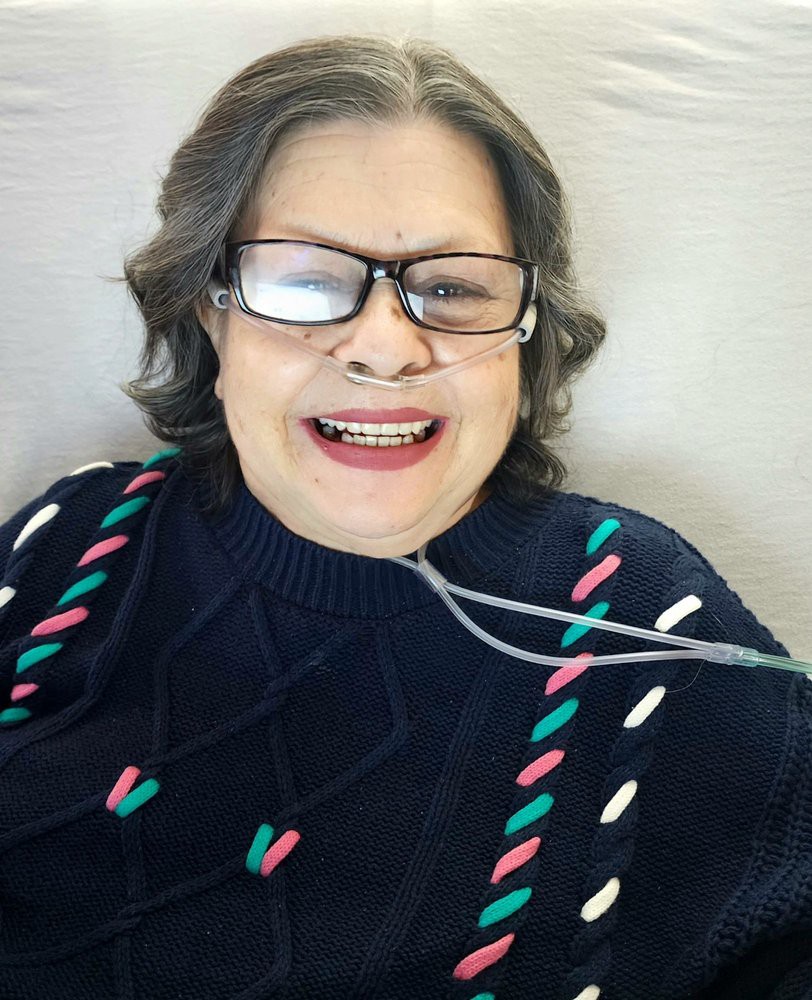 A smiling person wearing glasses and a sweater with an oxygen tube.