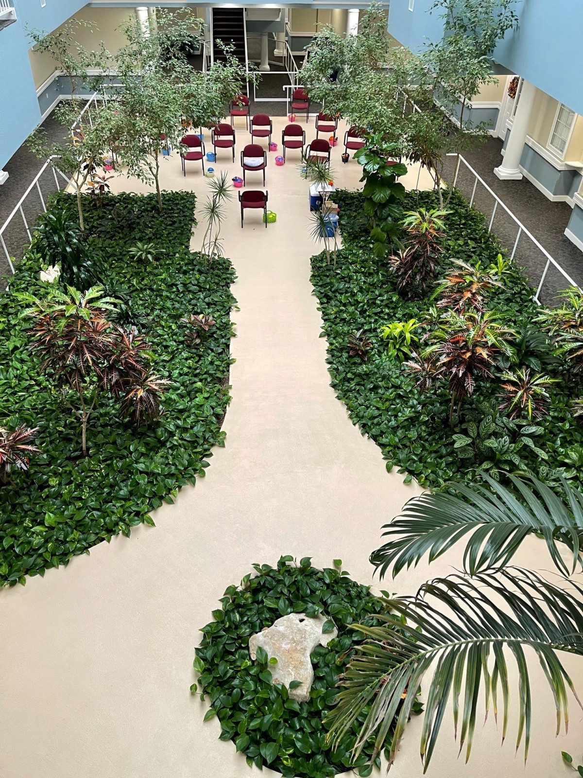 A serene indoor garden with a central pathway leading to a seating area with red chairs.