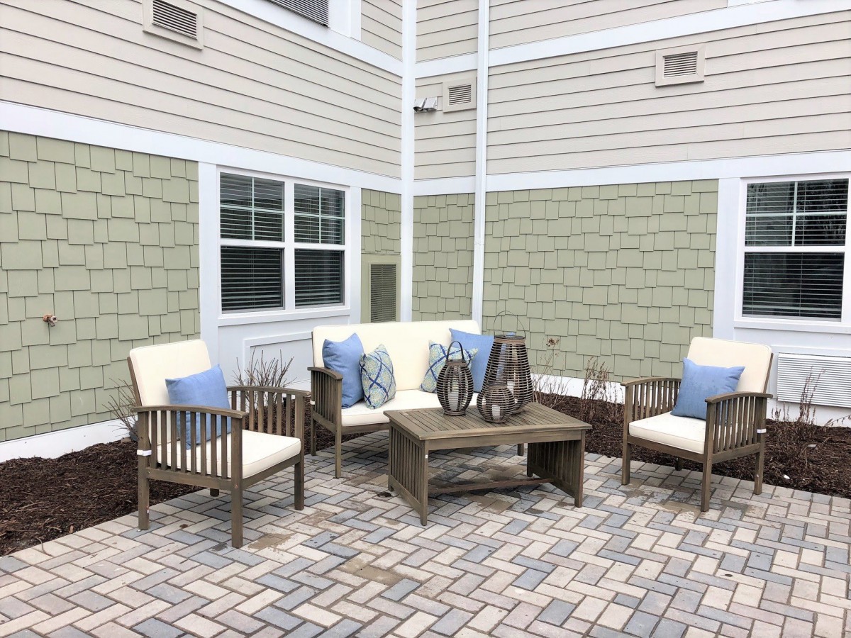 A cozy outdoor patio seating area with cushioned chairs and a coffee table on brick flooring.