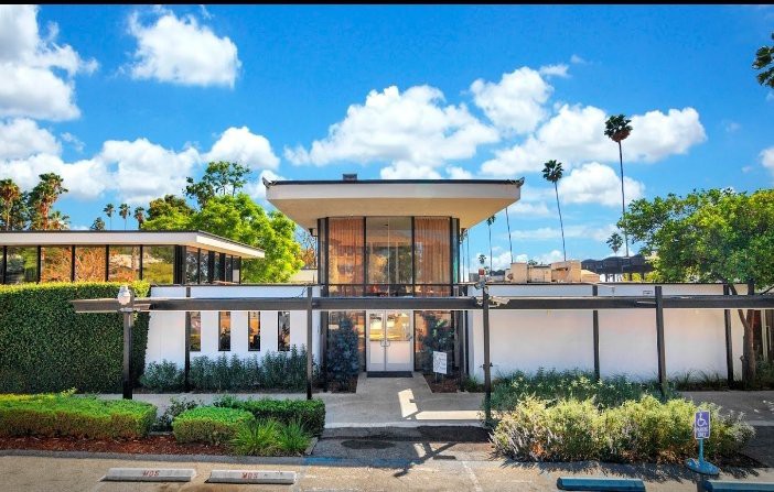 A modern mid-century style house with a landscaped yard under a bright blue sky.