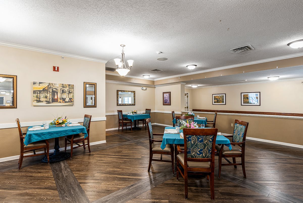 A well-lit dining room with neatly arranged tables and chairs, featuring warm decor and hardwood flooring.