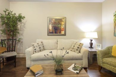 A cozy living room with a white sofa, decorative cushions, a wooden coffee table, and a lamp providing ambient lighting.