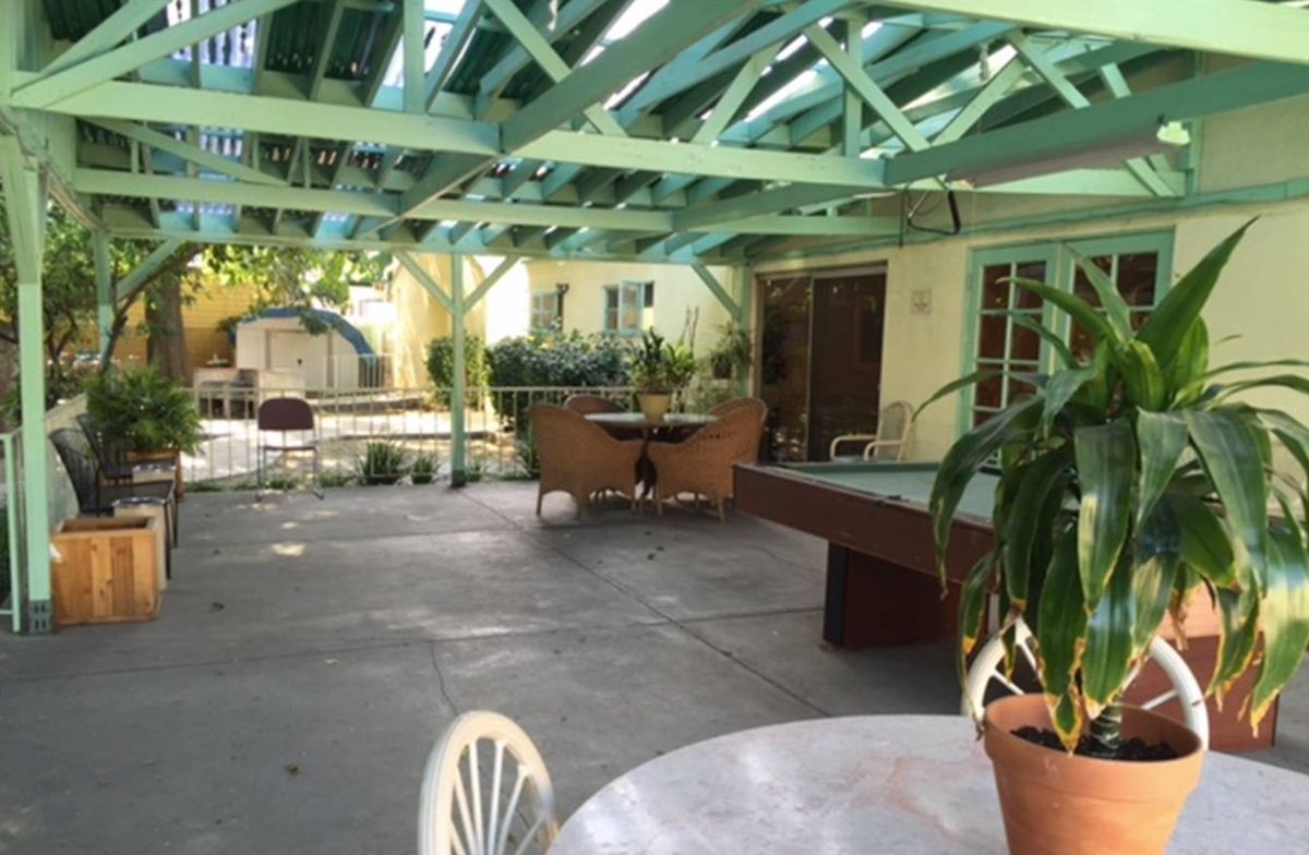 A sunny backyard patio with a pergola, outdoor furniture, and potted plants.