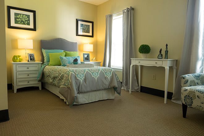 A cozy bedroom with a neatly arranged bed, soft lighting, and a small desk by the window.