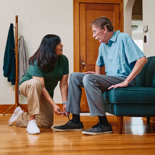 A caregiver assisting an elderly man with his shoe in a cozy home setting.