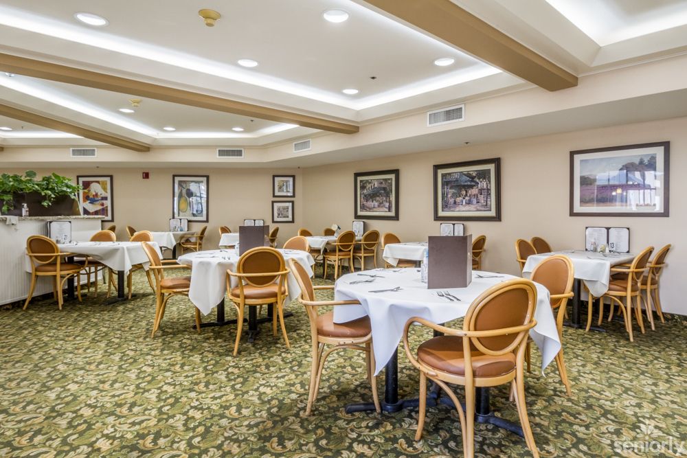 A neatly arranged dining area with tables and chairs, featuring decorated walls and a carpeted floor.