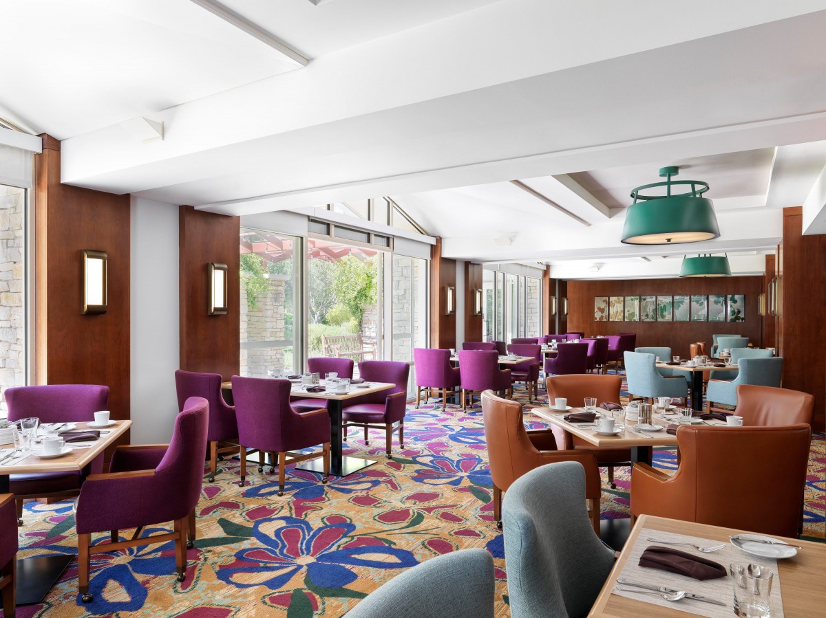 A modern restaurant interior with colorful carpet and ample seating, illuminated by natural light.