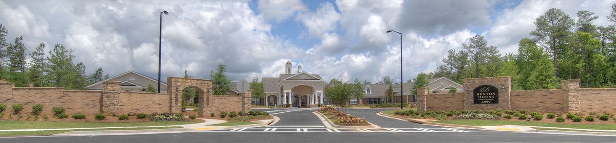 An elegant building with a grand entrance, surrounded by well-maintained landscaping under a cloudy sky.