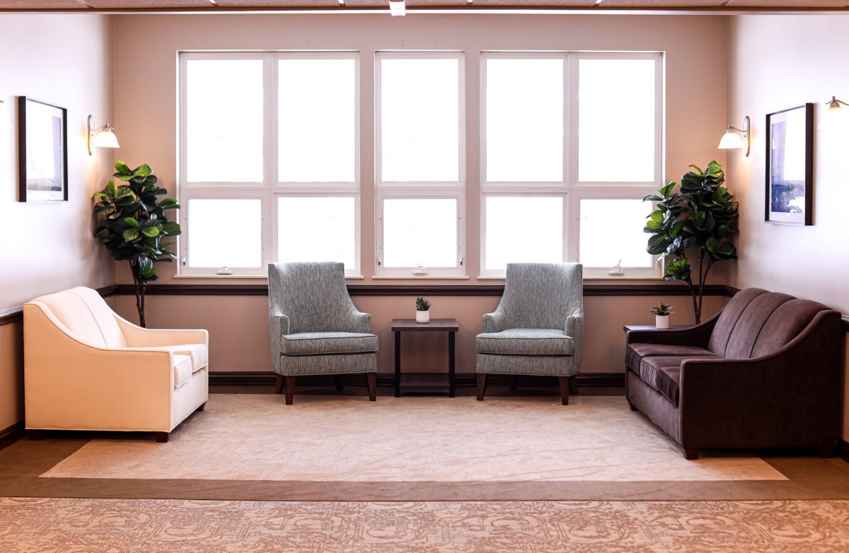 A cozy living room setup with two armchairs facing large windows, flanked by plants and a side table.