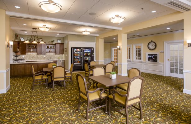A cozy dining area with tables and chairs, featuring warm lighting and a patterned carpet.