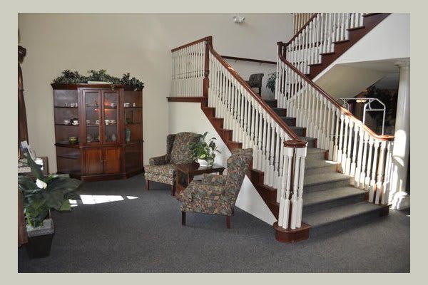 A cozy interior featuring a staircase, upholstered chairs, and a wooden cabinet.