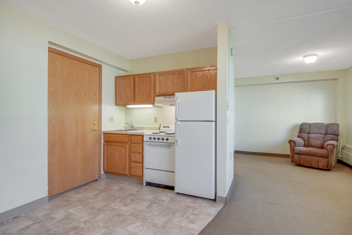 A small apartment kitchen with wooden cabinets, a refrigerator, and a stove.