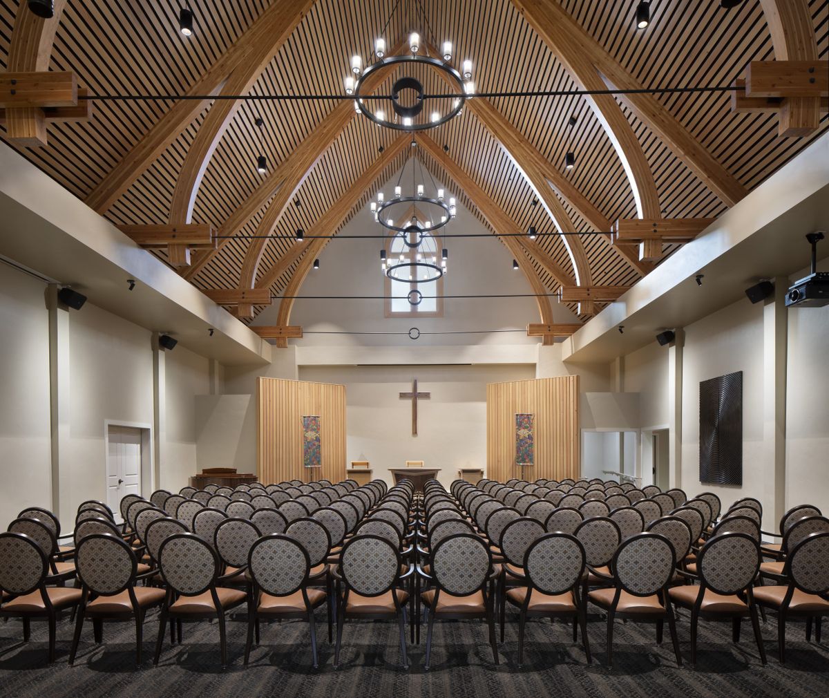 An elegant church interior with rows of seating and a wooden ceiling adorned with chandeliers.