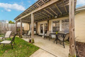 A cozy backyard patio with comfortable outdoor seating under a wooden pergola.