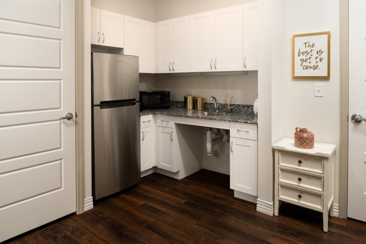 A modern kitchen featuring white cabinets, a stainless steel refrigerator, dark hardwood floors, and a microwave.