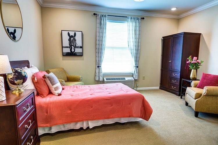 A cozy bedroom featuring a single bed with a coral bedspread, a framed artwork on the wall, and a window with curtains allowing natural light to fill the room.