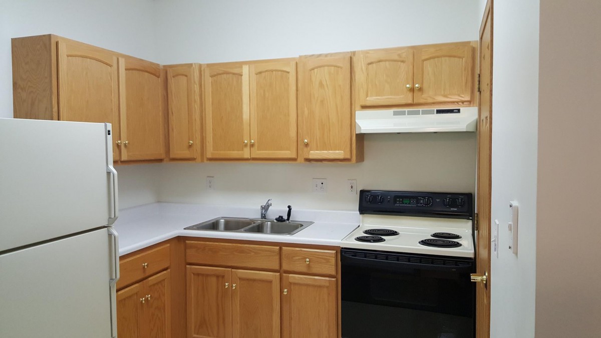 A modern kitchen with wooden cabinets, electric stove, and a double sink.