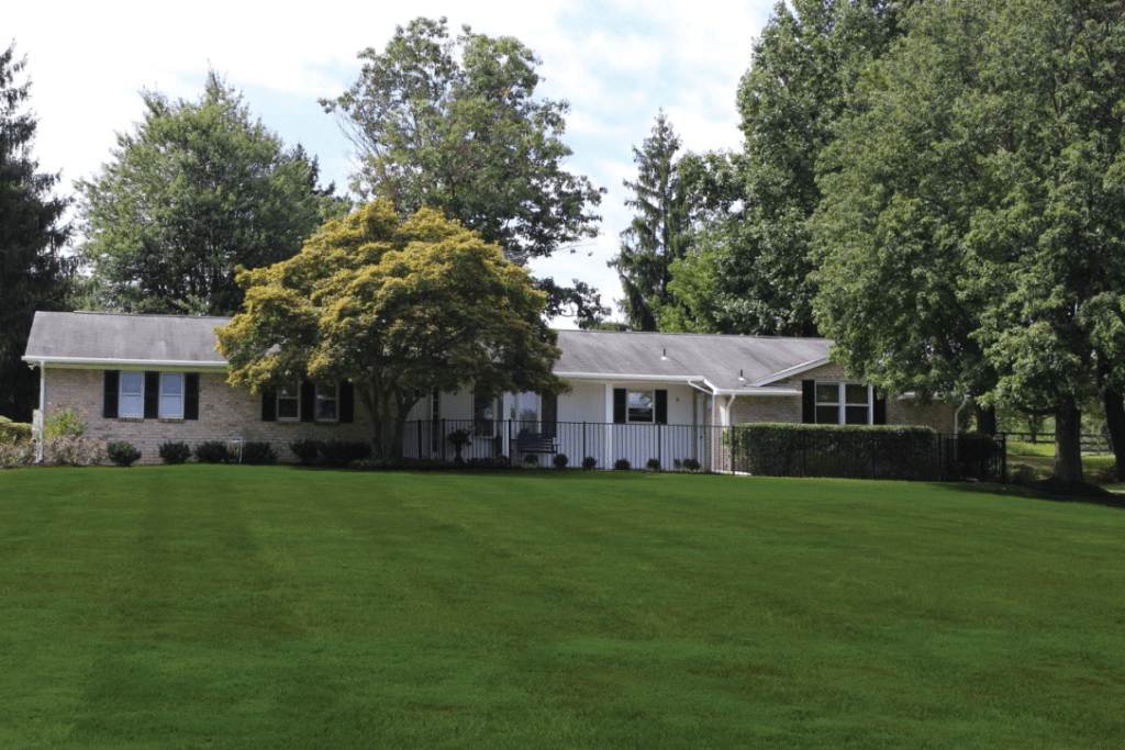 A one-story house with a large, well-maintained lawn and surrounding trees.