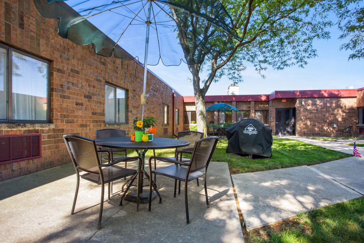 A cozy outdoor patio area with a table, chairs, and an umbrella next to a brick building.
