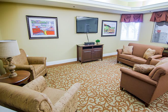 A cozy living room featuring a sofa, armchairs, a television, and framed artwork on the walls.