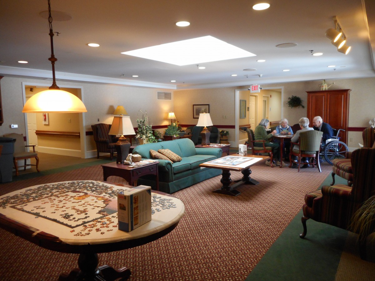 A cozy living room with comfortable seating and a table, featuring people gathered in conversation under warm lighting.
