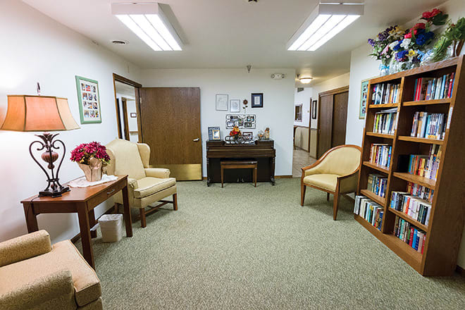 A neatly organized waiting room with comfortable chairs, a piano, and bookshelves.