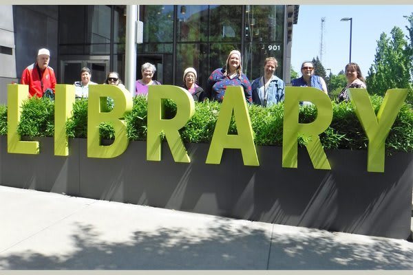 Group of people standing behind large 'LIBRARY' sign outside a building.