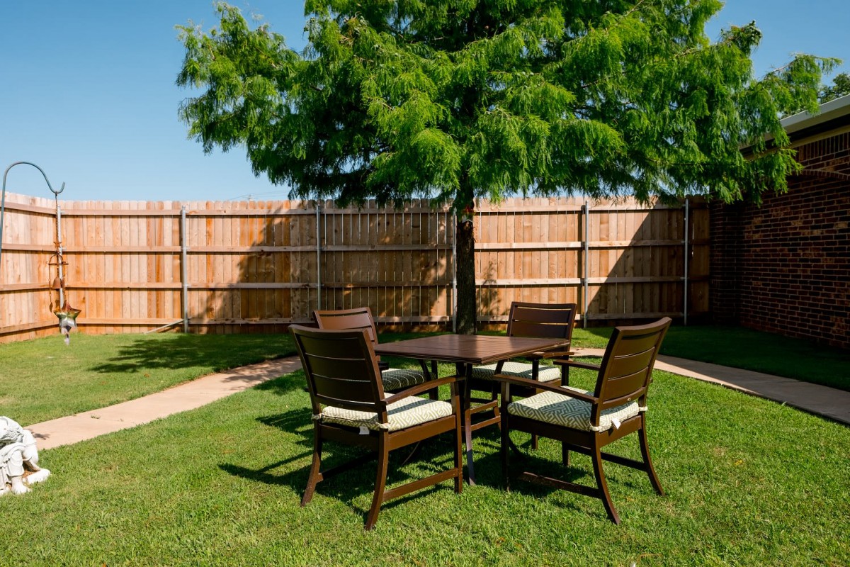 A set of outdoor furniture on a grassy backyard with a tree and wooden fence.