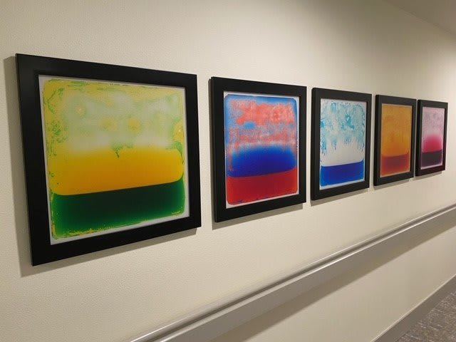 A row of abstract, colorful paintings displayed in a gallery.